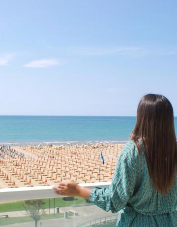 Woman gazes at the sea from a balcony, beach with umbrellas.