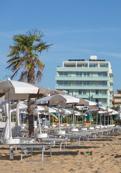 Beach with umbrellas and sunbeds, palm trees and buildings in the background.