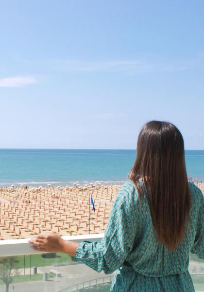 Woman gazes at the sea from a balcony, beach with umbrellas.