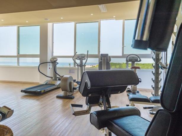 Palestra moderna con vista mare, attrezzature fitness e grandi finestre.