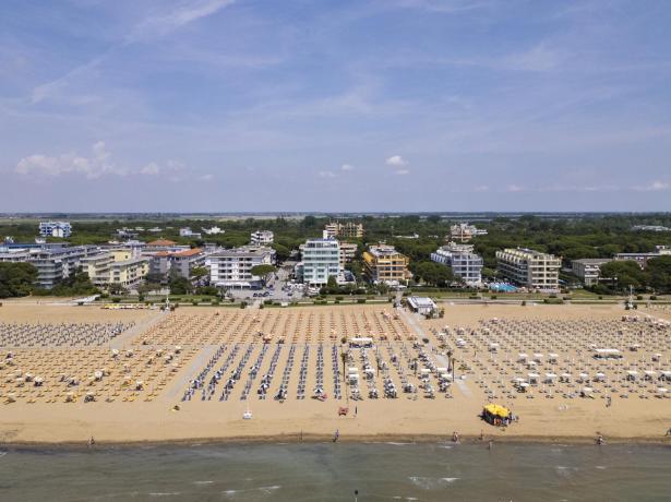 Strand mit Sonnenschirmen und Gebäuden im Hintergrund, sonniger Tag.