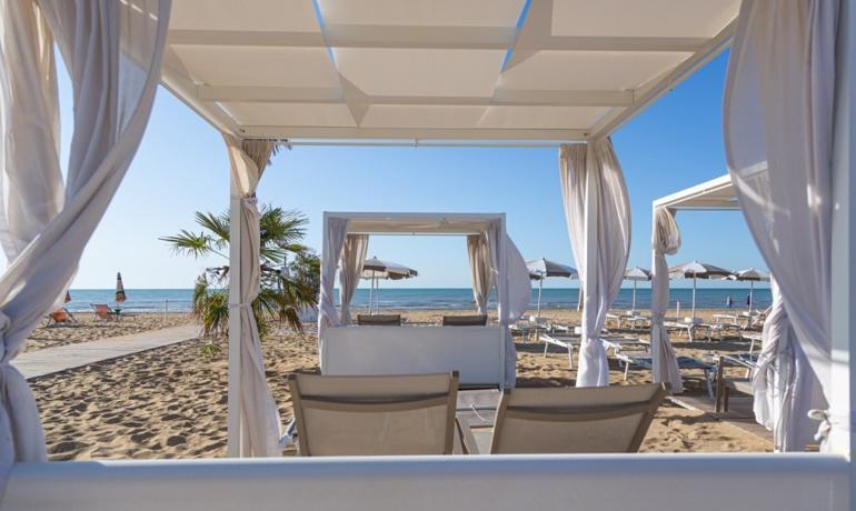 Beach with loungers under white gazebos, calm sea.