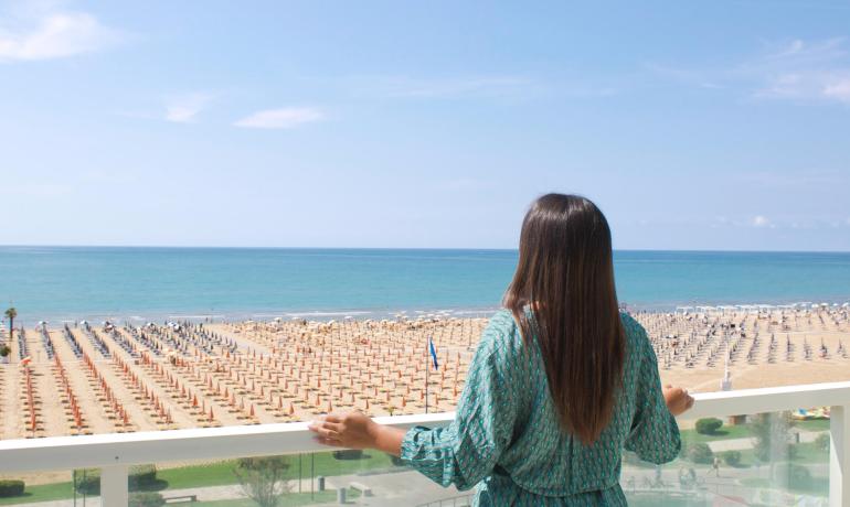 Woman gazes at the sea from a balcony, beach with umbrellas.