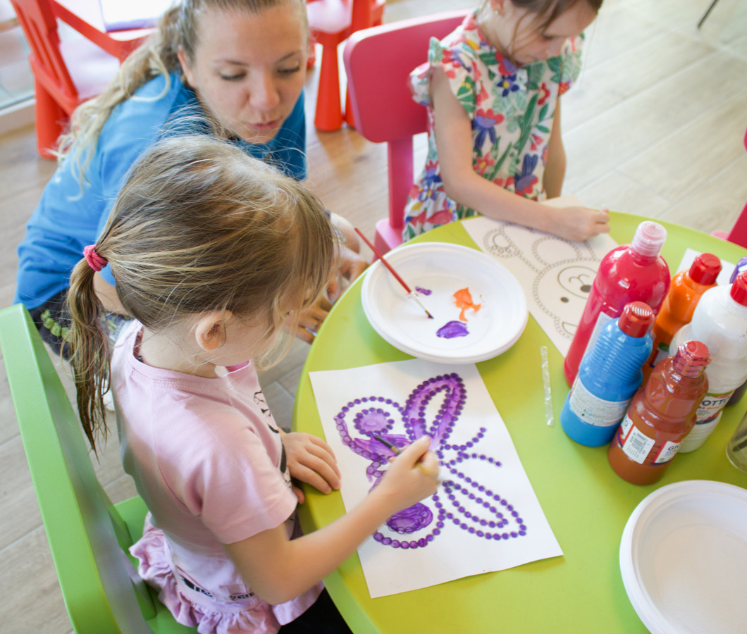 Children painting with bright colors on a green table.