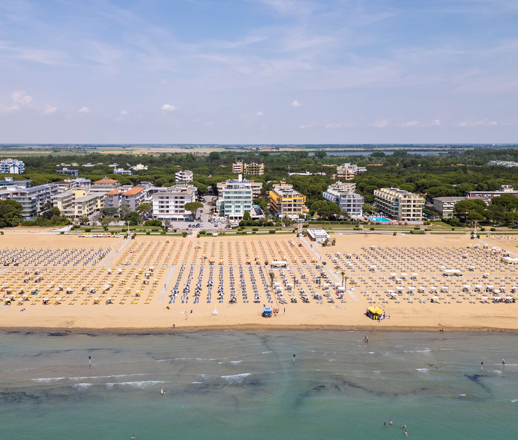 Spiaggia con ombrelloni e edifici sullo sfondo, vista dall'alto in una giornata soleggiata.