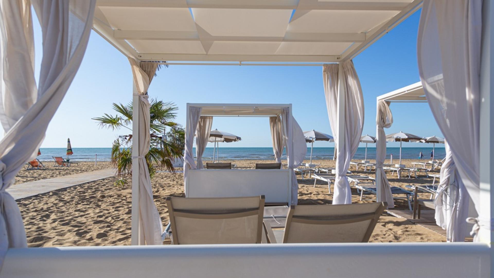 Sandy beach with loungers and white canopies, calm sea in the background.