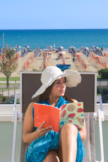 Woman reading on the beach with a white hat.